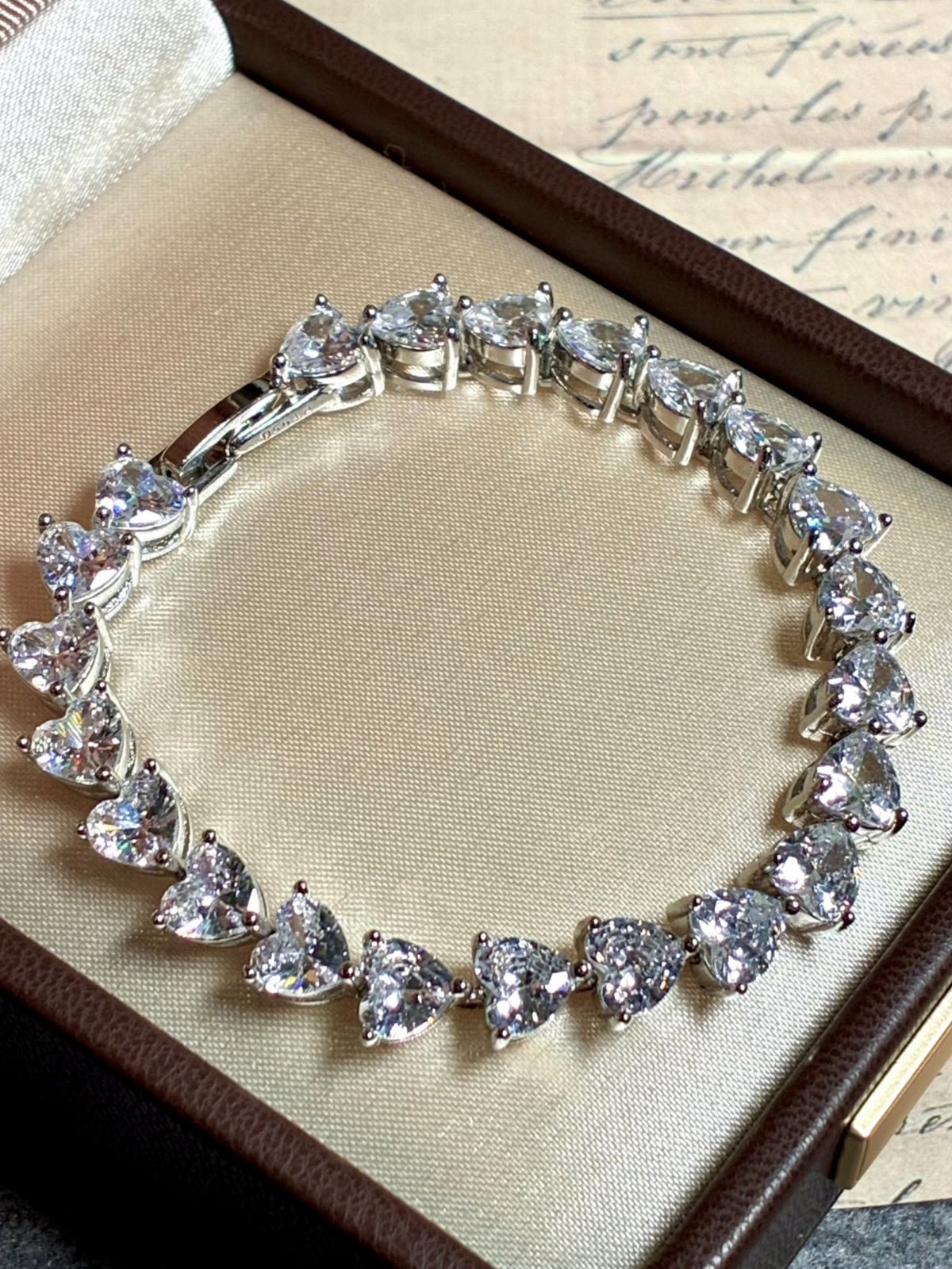 The Social Queen Heart-Shape Crystal Bracelet, featuring heart-cut crystals in a silver-tone, is beautifully presented in a beige jewelry box—ideal for elegant wedding guest jewelry.