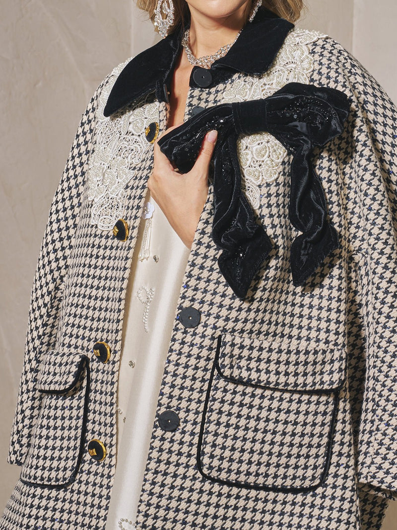 A person wearing the Social Queen Houndstooth Tweed Bow Jacket, featuring a black velvet bow detail, lace accents, black collar, and large buttons. Only the lower face and upper body are visible.