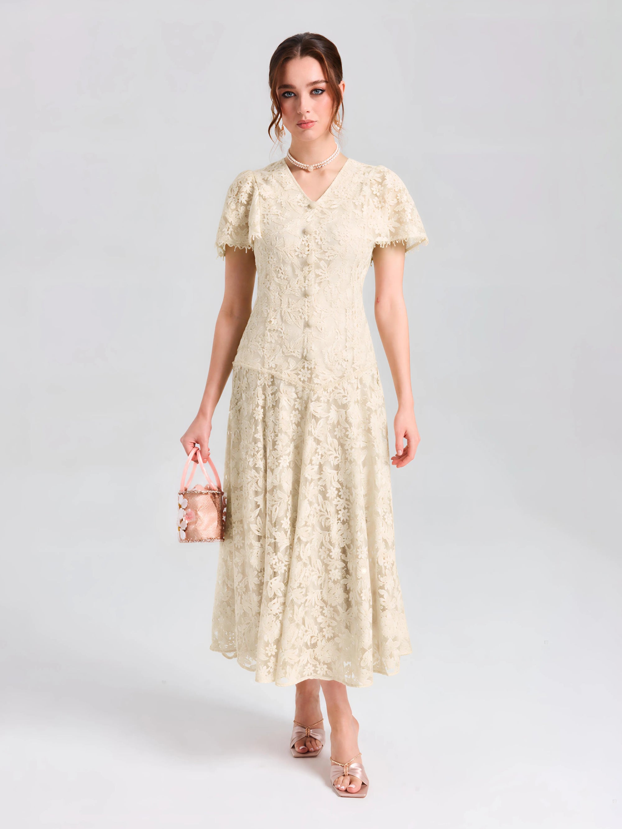 A woman wears the Social Queen Floral Embroidered Lace Dress—a cream A-line midi with short sleeves—paired with a small pink handbag, set against a plain light background.