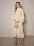 A woman wears the Social Queen Floral Appliqué Embroidered Ruffle Dress, holding a gold purse as she stands against a neutral textured wall with one foot slightly forward.