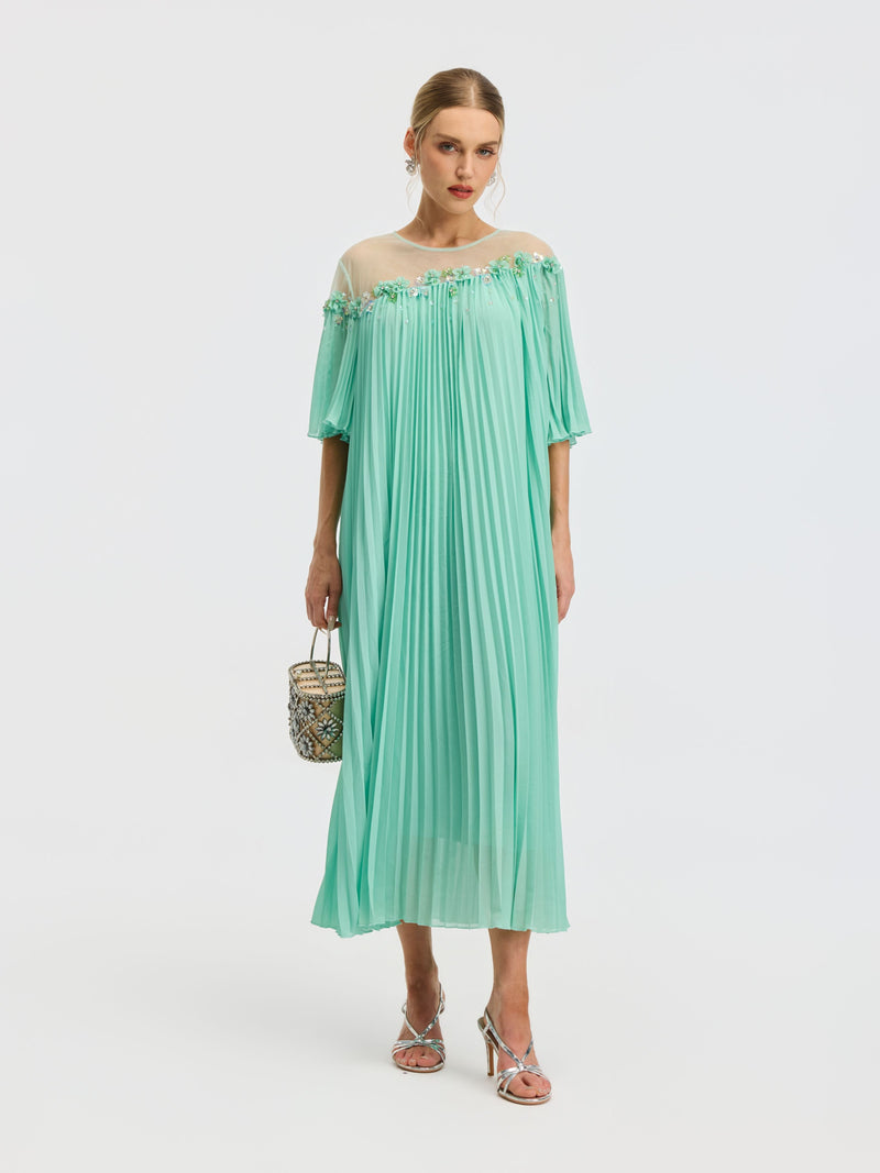 Model wears the Social Queen Floral Embellishment Pleated Dress, featuring a loose pleated mesh silhouette in mint green with beaded floral details at the neckline, styled with silver heels and a small patterned handbag against a white background.