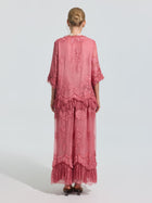 A person faces away, wearing the Social Queen 3D Floral Embroidered 100% Silk Ruffle Blouse in pink with floral embroidery and ruffled hem, set against a plain light background.