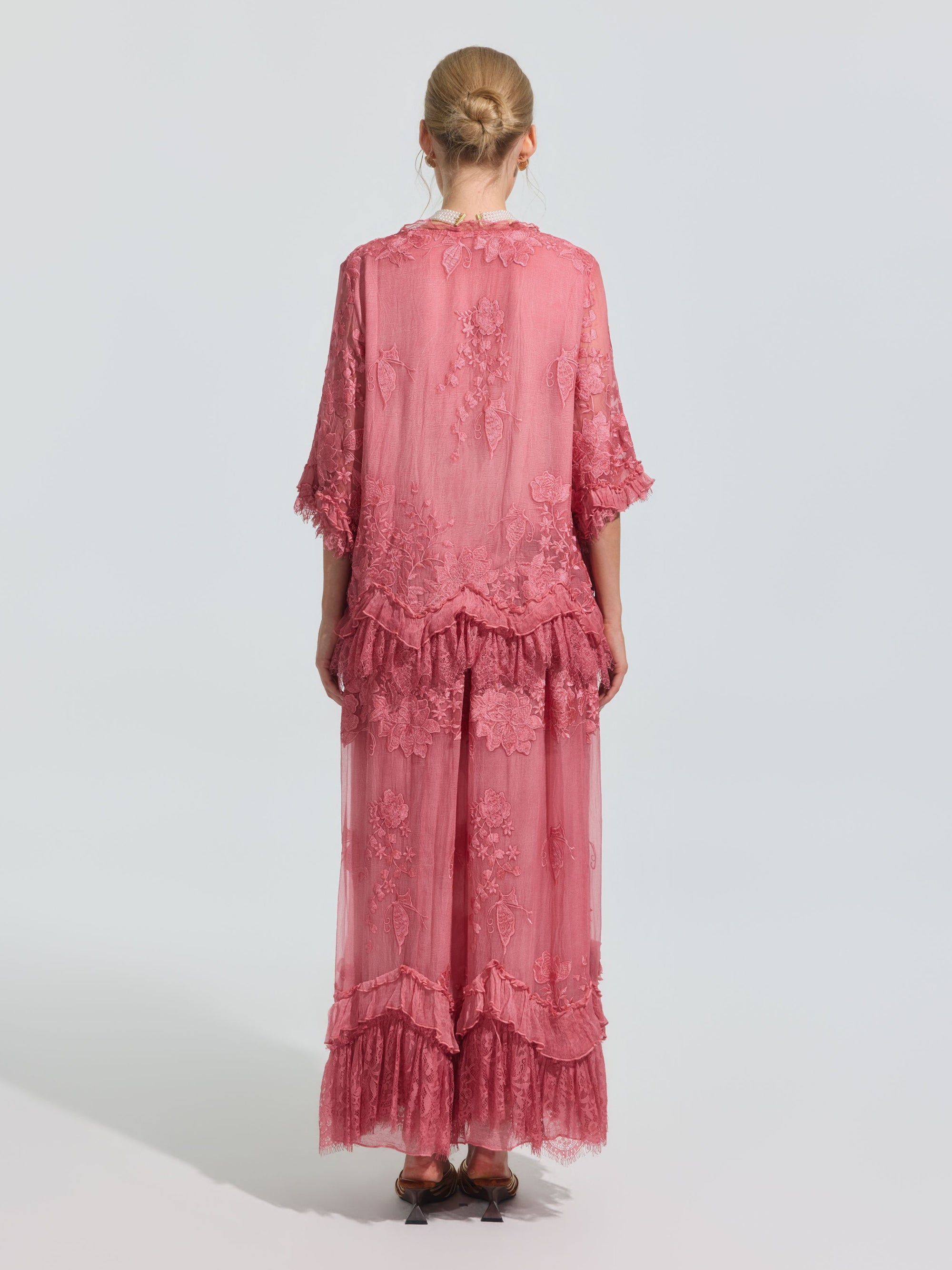 A person faces away, wearing the Social Queen 3D Floral Embroidered 100% Silk Ruffle Blouse in pink with floral embroidery and ruffled hem, set against a plain light background.