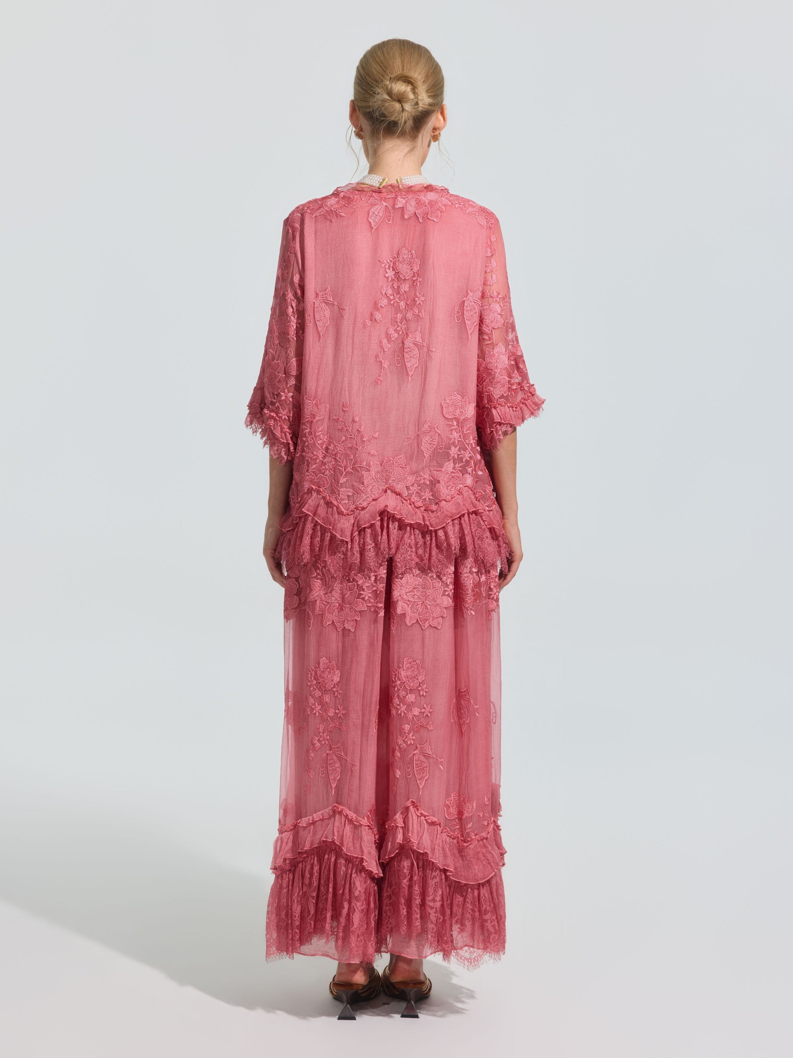 A person faces away, wearing the Social Queen 3D Floral Embroidered 100% Silk Ruffle Blouse in pink with floral embroidery and ruffled hem, set against a plain light background.