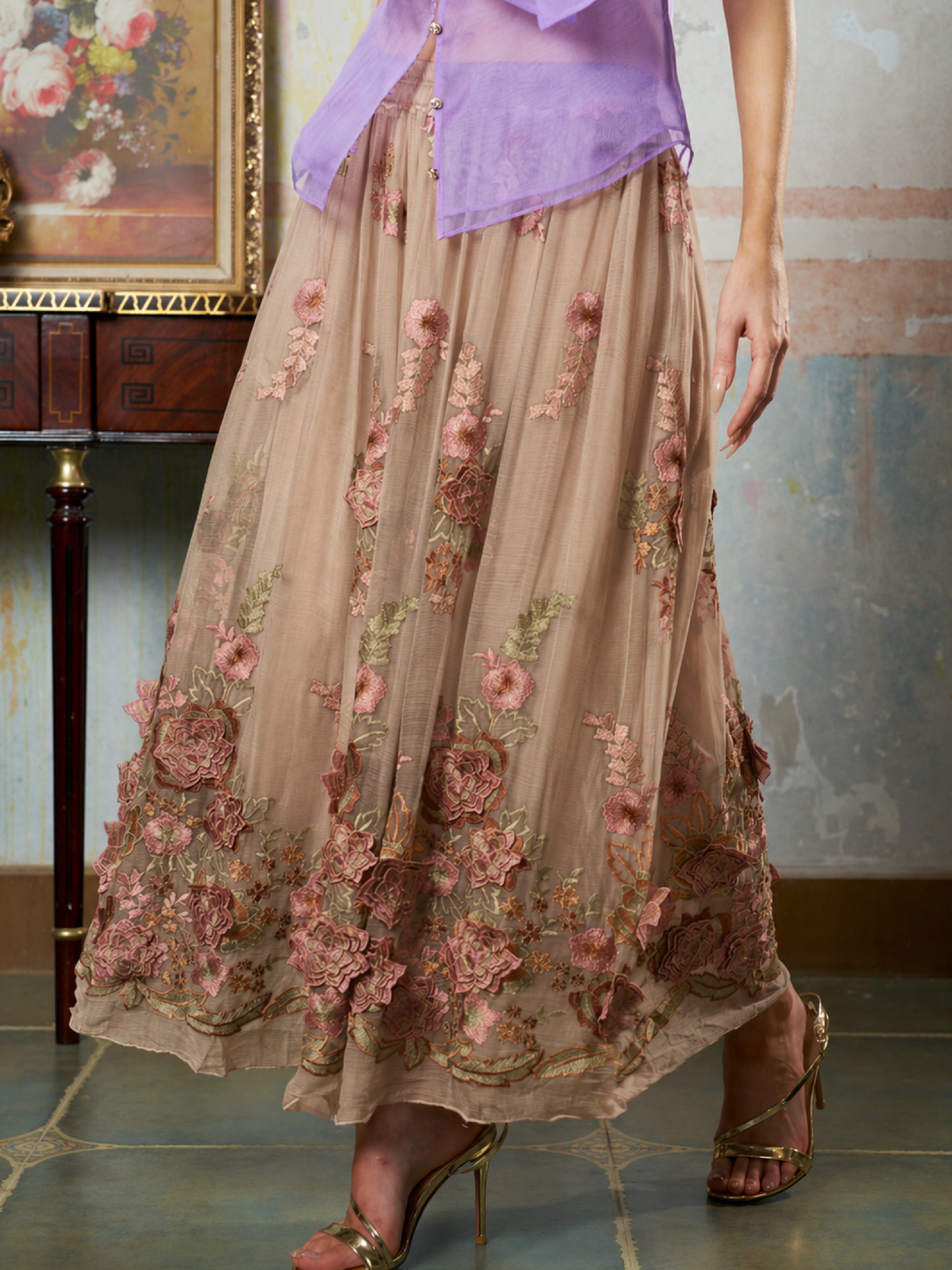A person wearing a light purple blouse and the Social Queen 3D Floral Embroidered Silk Skirt, paired with gold high-heeled sandals.