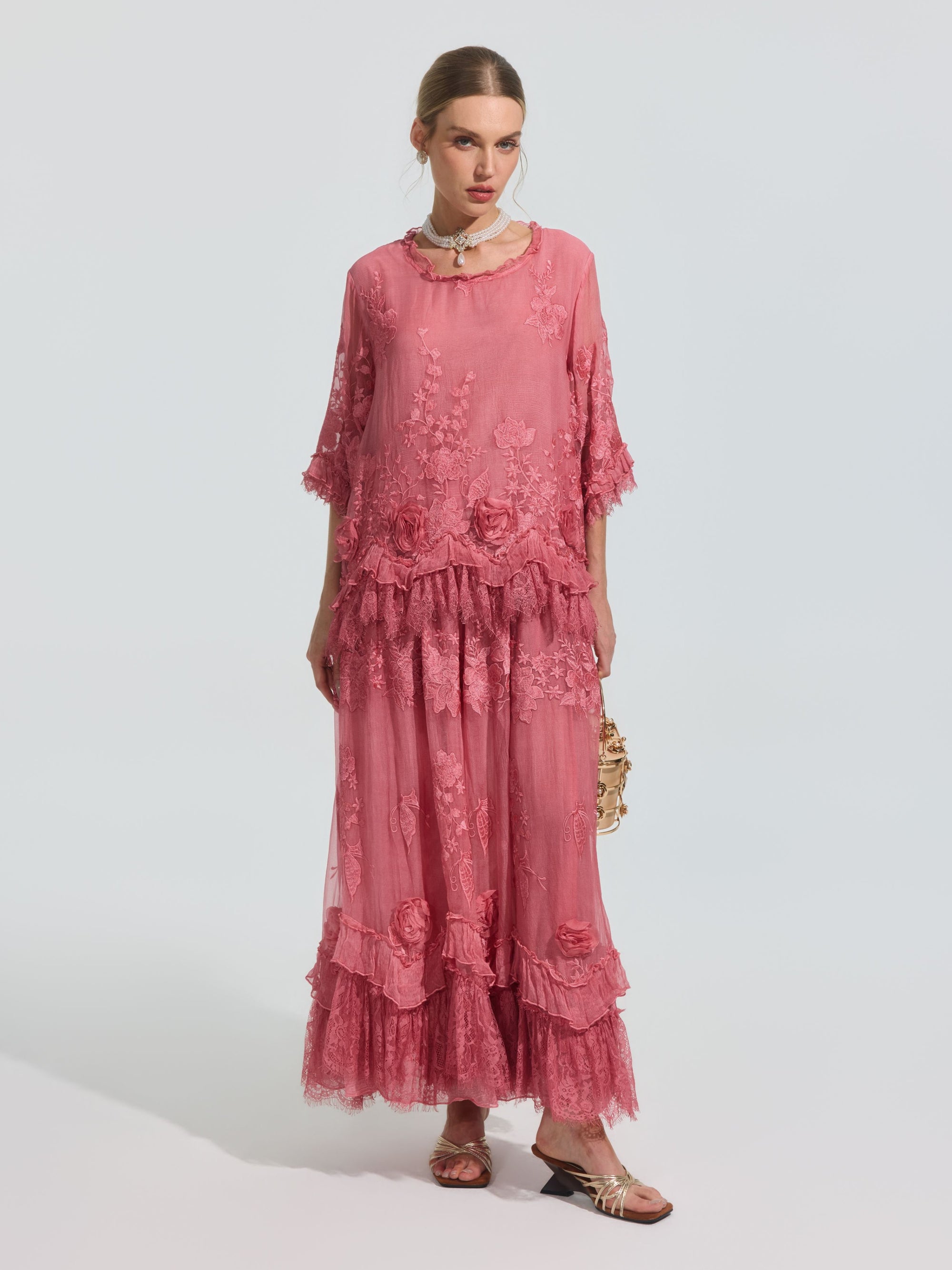 A woman wears the Social Queen 3D Floral Embroidered 100% Silk Ruffle Blouse, featuring floral embroidery and ruffle details, paired with a small purse and sandals against a plain background.