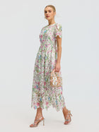 A woman in the Social Queen Botanical Embroidered Cutout Dress and silver heels carries a decorative handbag, walking against a plain light background.
