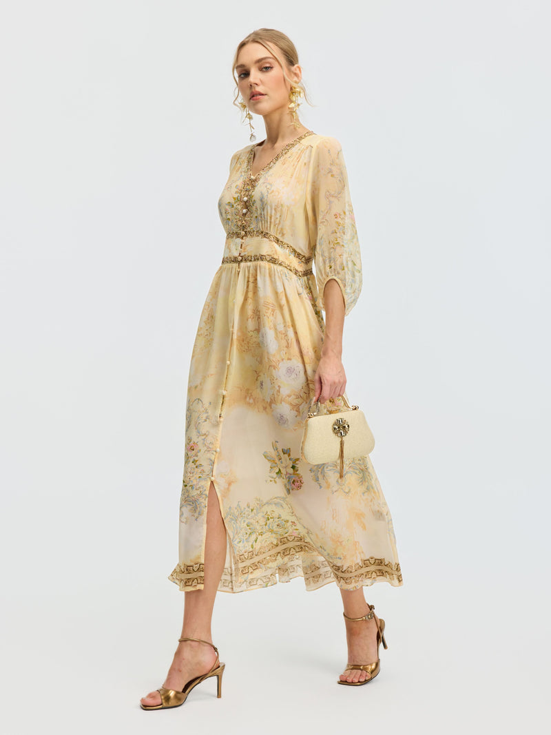 Woman in a Social Queen Floral Silk V-Neck Beaded Dress with sheer sleeves, carrying a small cream handbag and wearing gold sandals, walking against a plain white background.
