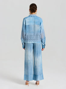 A woman faces away, wearing Social Queen's Washed Silk Wide-Leg Pants in light blue, featuring an elastic drawstring waistband and a relaxed silhouette, paired with beige heels.