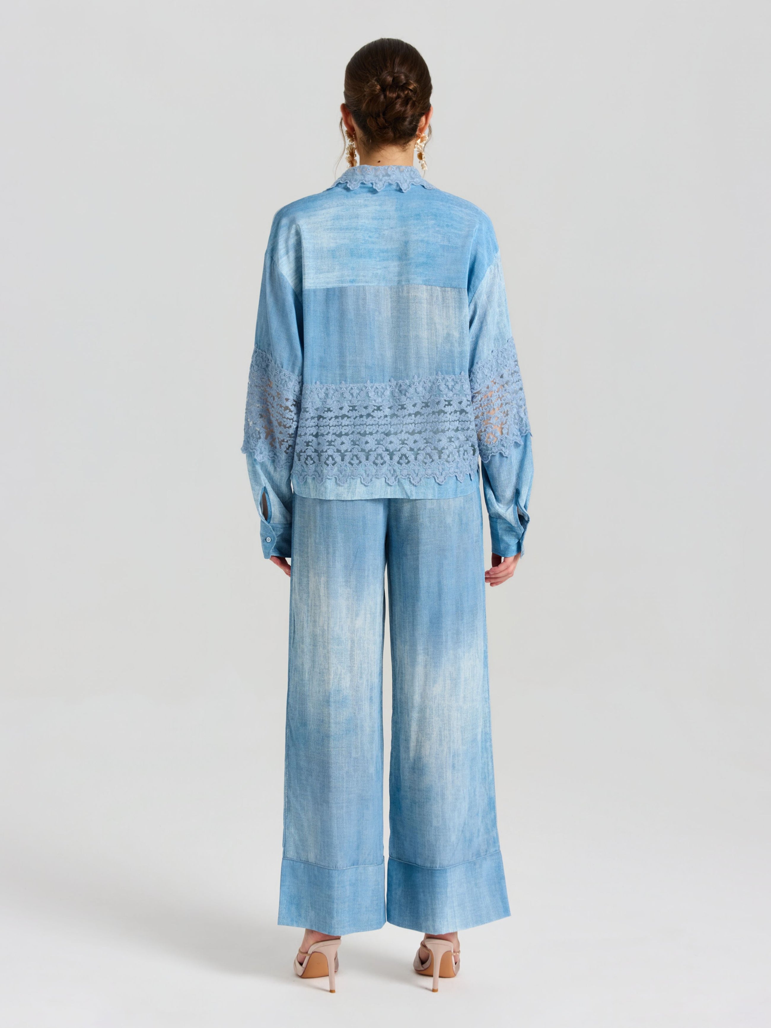 A woman faces away, wearing Social Queen's Washed Silk Wide-Leg Pants in light blue, featuring an elastic drawstring waistband and a relaxed silhouette, paired with beige heels.