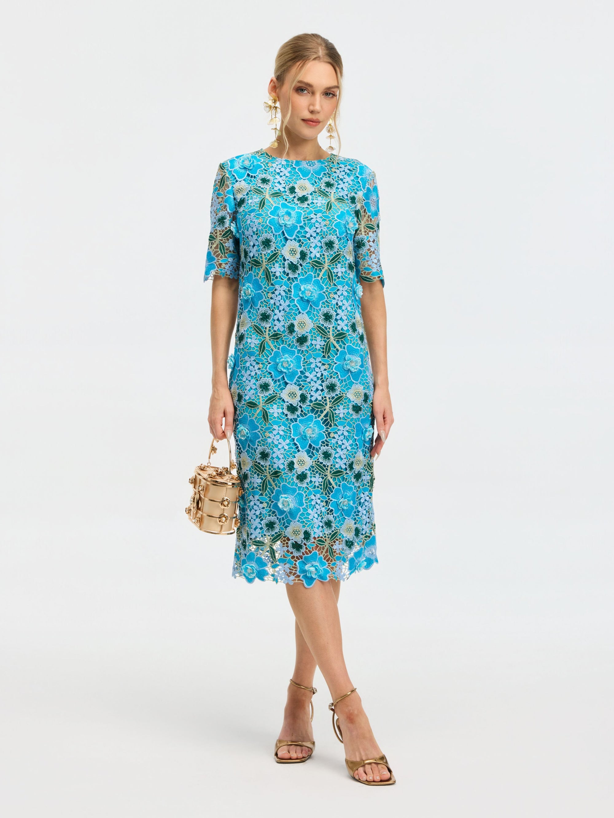 A woman wears the Social Queen Floral Appliqué Lace Shift Dress with short sleeves, paired with a beige handbag and strappy sandals, standing against a plain white background.