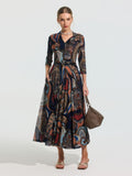 A woman wears the Social Queen Paisley Print Knit Dress (Belt Included), featuring long sleeves and a colorful paisley pattern, paired with sandals and a brown woven handbag.
