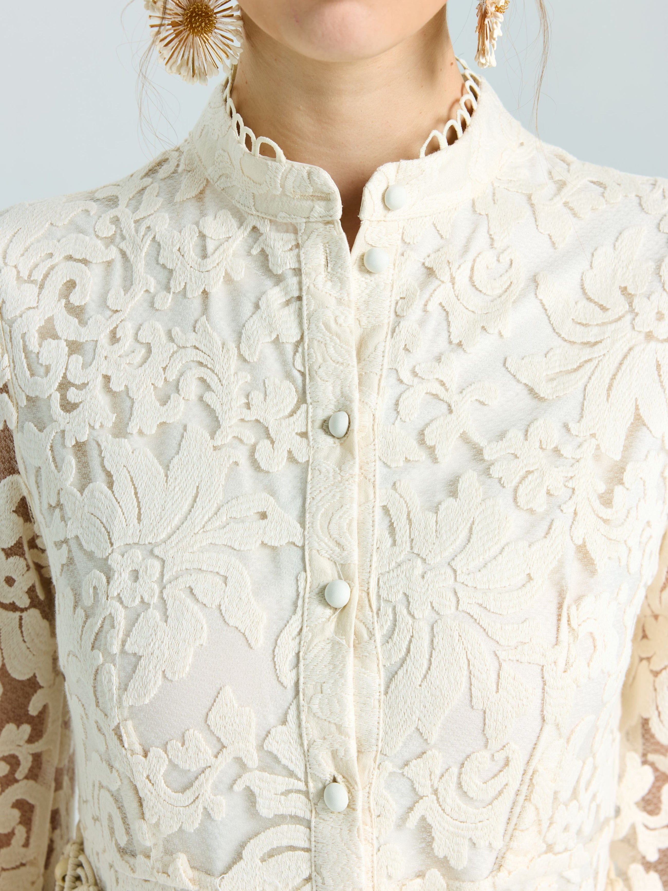 Close-up of a woman wearing the Embroidered Lace High-Neck Dress by Social Queen, featuring cream-colored lace-effect embroidery, decorative buttons, and styled with large textured gold earrings.