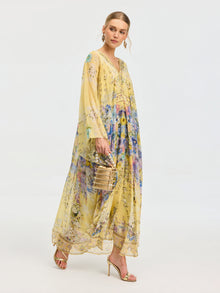 A woman in the Social Queen Floral Print Silk Caftan Dress with gold heels and a beige handbag stands against a plain backdrop—an ideal resort look.