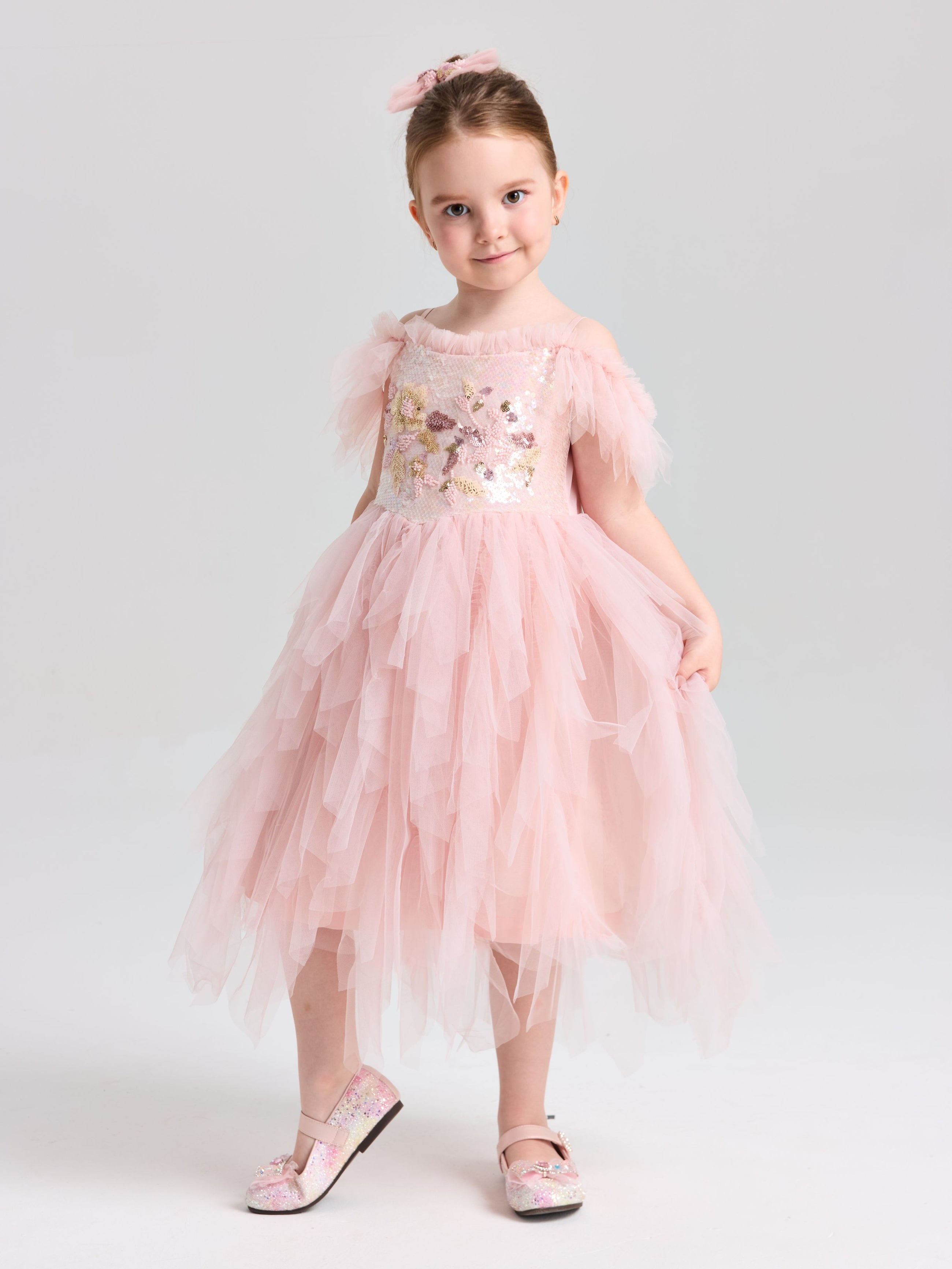A young girl wears the Social Queen Girls Floral Sequin Tulle Dress with matching pink shoes, posing against a plain light background.