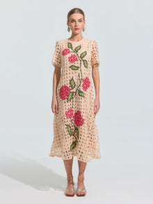 A woman models the Social Queen Hydrangea Embroidered Openwork Dress, a light beige, knee-length piece featuring geometric cutouts and pink-green floral embroidery, paired with sandals against a plain light background.