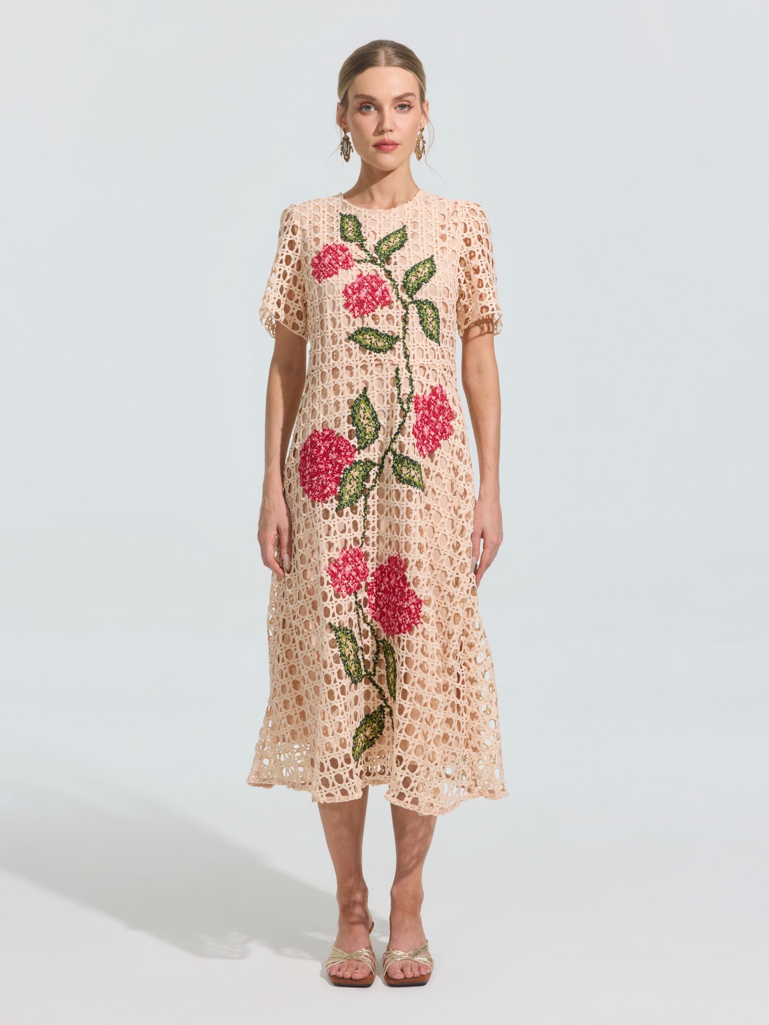 A woman models the Social Queen Hydrangea Embroidered Openwork Dress, a light beige, knee-length piece featuring geometric cutouts and pink-green floral embroidery, paired with sandals against a plain light background.