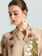 A woman wearing a beige embroidered top with gold and white sequin details, a gold chain necklace, and Social Queen’s Daisy Cluster Earrings, looks down against a plain background.