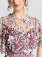 A woman wears the Social Queen Floral Beaded A-Line Dress, featuring a sheer, embroidered overlay with blue, purple, and cream floral appliqués. Only her head and upper body are visible.