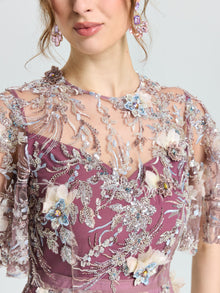 A woman wears the Social Queen Floral Beaded A-Line Dress, featuring a sheer, embroidered overlay with blue, purple, and cream floral appliqués. Only her head and upper body are visible.