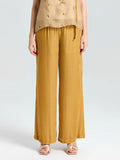 A person shown from chest to feet wears a sleeveless beige top and Social Queen Silk Velvet Wide-Leg Pants in mustard yellow with gold open-toe sandals, posed against a plain background.