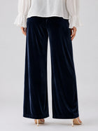 A person is shown from the back wearing Social Queen’s Silk Velvet Wide-Leg Pants in navy blue, paired with a white long-sleeve blouse featuring ruffled cuffs and beige heeled sandals.