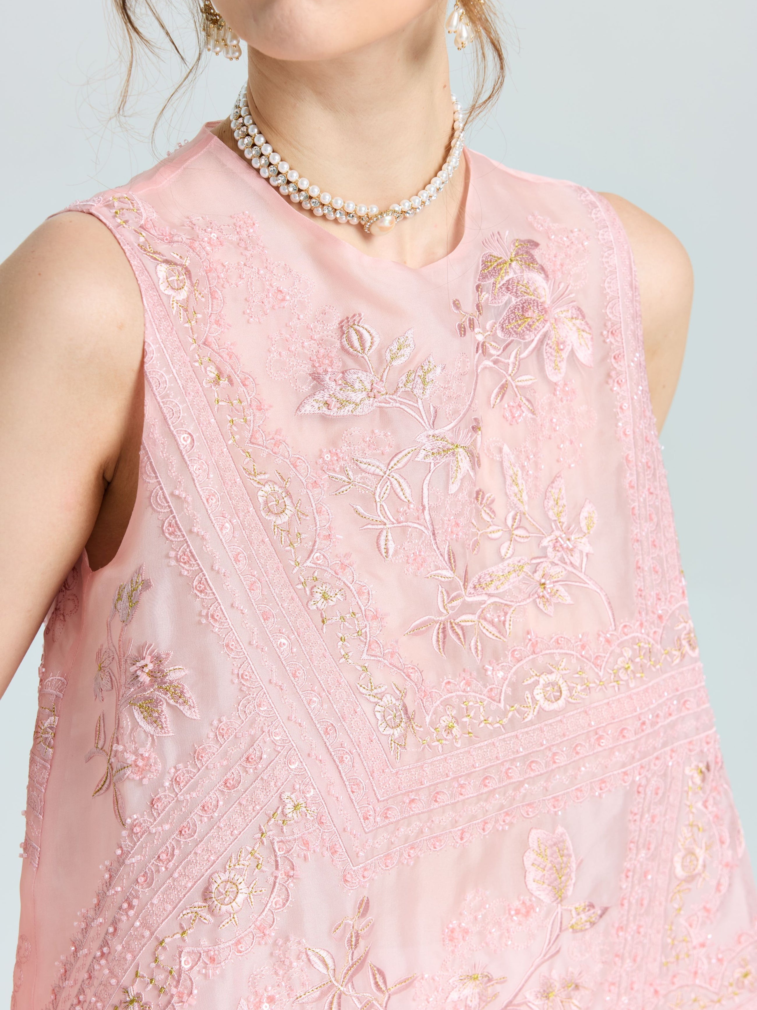 A woman wears the Social Queen Floral Bird Embroidered Silk Top featuring intricate floral embroidery, styled with layered pearl necklaces.