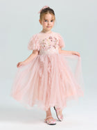 A young girl wears the Social Queen Girls Sequin Embellished Tulle Dress, featuring a light pink princess design with floral details, matching shoes, and a bow in her hair, posing against a plain light background.