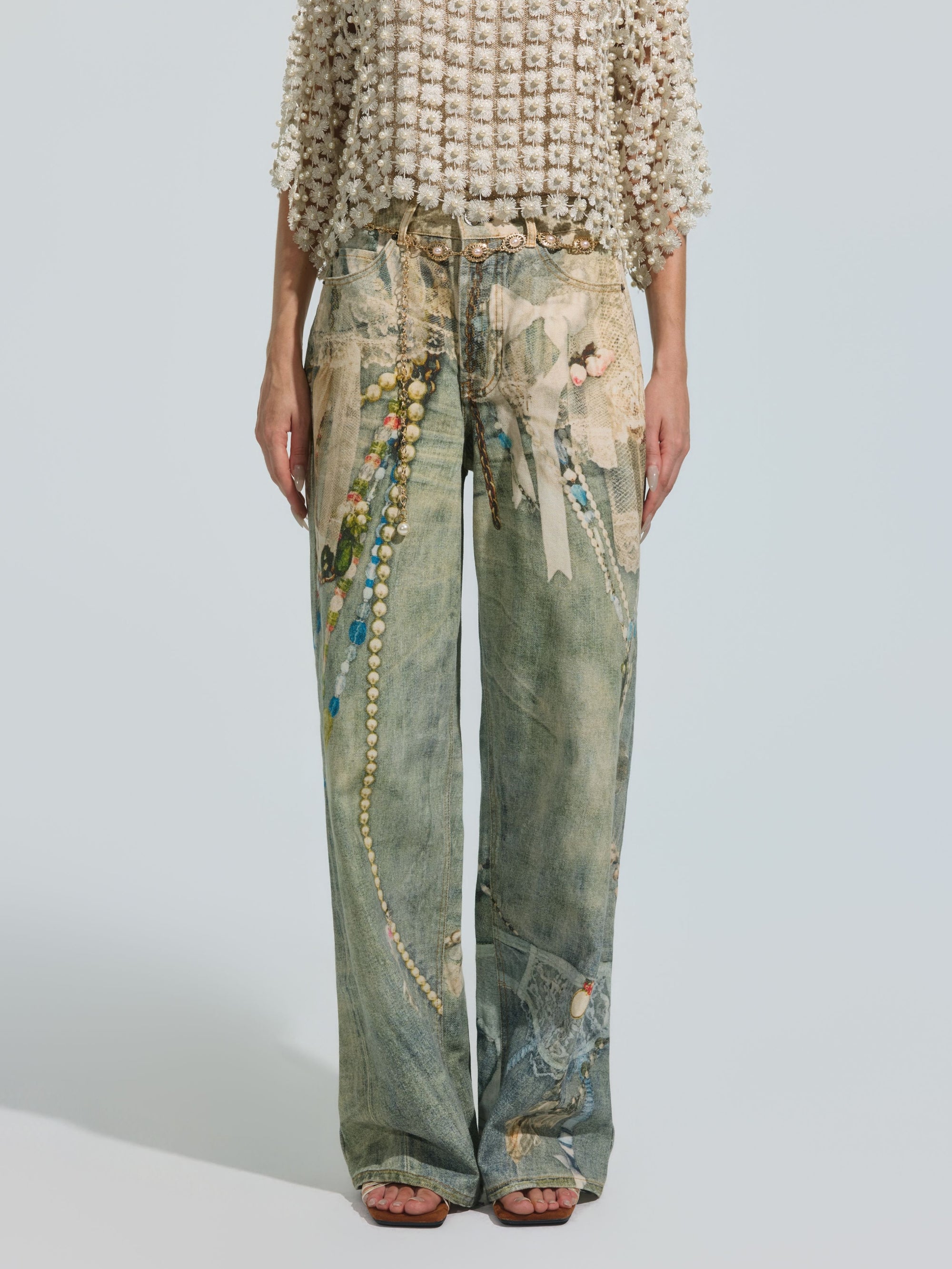 A person is shown from the shoulders down, against a plain background, wearing a textured short-sleeve top paired with Social Queen’s Pearl Chain Printed Jeans—washed denim featuring a colorful, beaded-inspired pattern in a wide-leg silhouette.