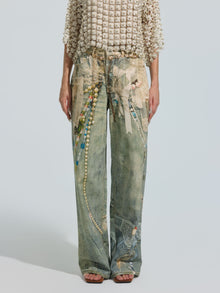 A person is shown from the shoulders down, against a plain background, wearing a textured short-sleeve top paired with Social Queen’s Pearl Chain Printed Jeans—washed denim featuring a colorful, beaded-inspired pattern in a wide-leg silhouette.