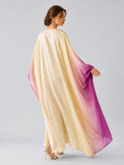 A woman stands with her back to the camera against a plain light background, wearing Social Queen’s Ombré Beaded Embroidered Cape Dress—a flowing maxi silhouette with long sleeves and a gradient that transitions from cream to purple.