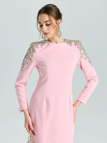 A woman in the Social Queen Crystal Beaded Detail Midi Dress—featuring long sleeves, light pink crepe fabric, and crystal shoulder accents—looks down with a chic low updo, ideal for elegant evening occasions.