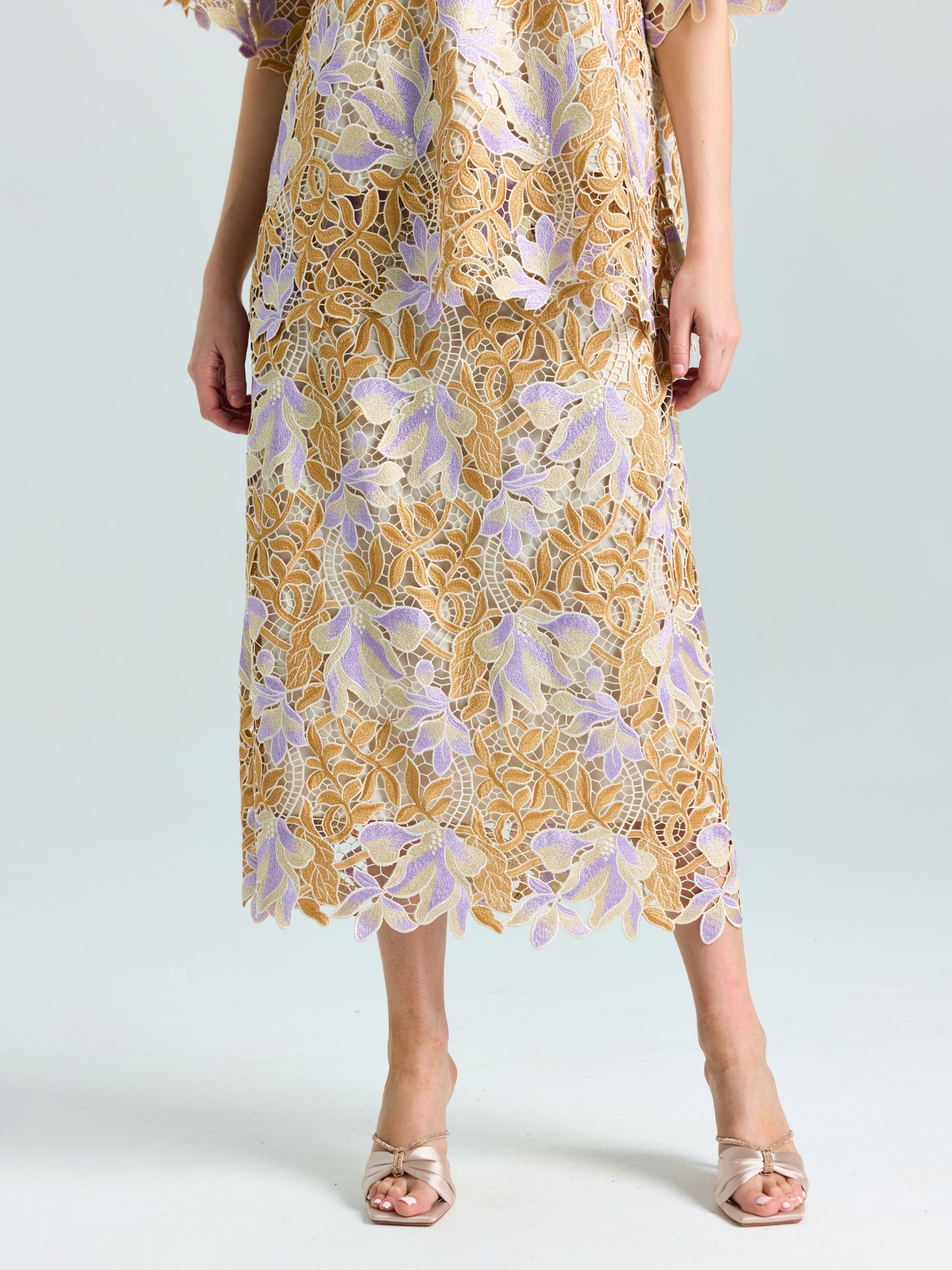 Wearing the Social Queen Floral Embroidered Lace Midi Skirt in gold and lavender with scalloped hem, paired with open-toe heels—ideal for evening occasions against a plain background.