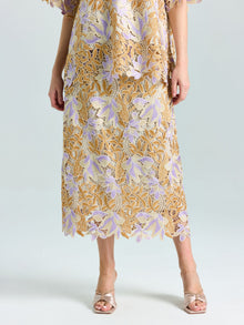 Wearing the Social Queen Floral Embroidered Lace Midi Skirt in gold and lavender with scalloped hem, paired with open-toe heels—ideal for evening occasions against a plain background.