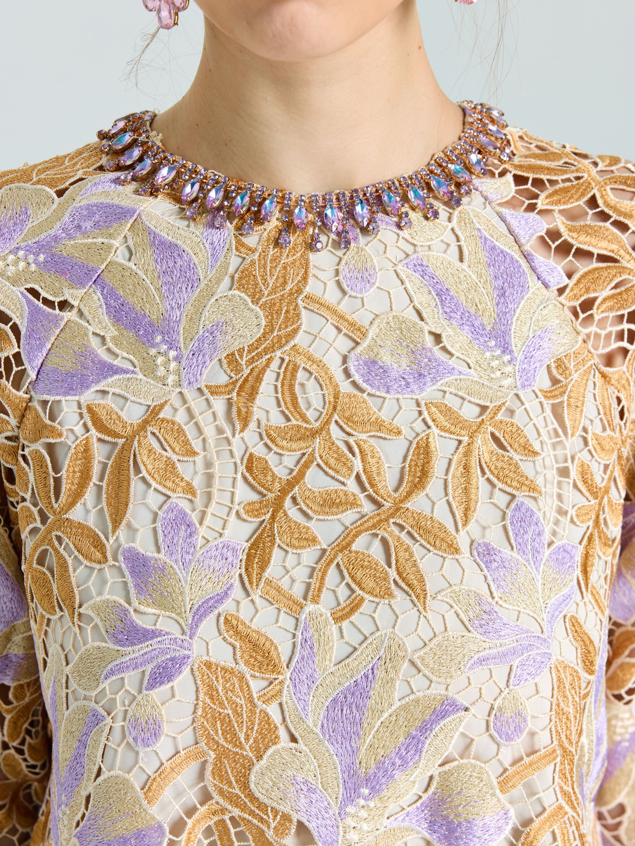 A person wears the Social Queen Floral Embroidered Lace Top with gold and lavender details, paired with a beaded necklace of purple and clear stones.