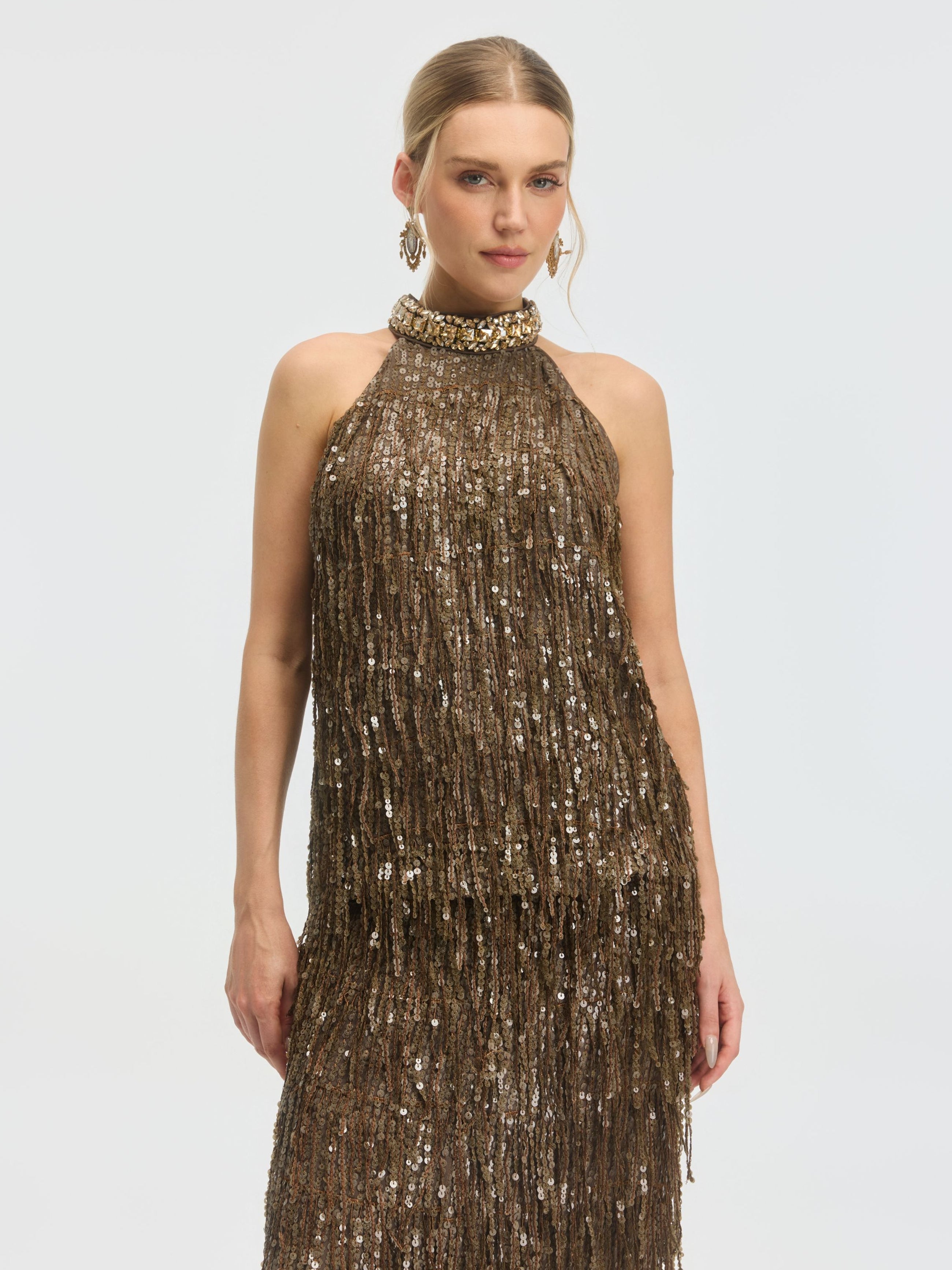 A woman wears the Social Queen Beaded Sequin Fringe Halter Top, featuring a sleeveless design with shimmering sequins and fringe, standing against a plain light background.