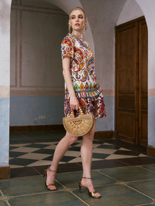A woman in the Paisley Garden Print Silk Top by Social Queen and gold heels carries a bamboo handbag as she walks indoors on patterned tile flooring, capturing the effortless elegance of resort wear.