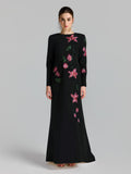 A woman models the Social Queen Floral Beaded A-Line Gown, featuring long sleeves with pink floral appliqué and green leaf embroidery, set against a plain light background.
