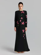 A woman models the Social Queen Floral Beaded A-Line Gown, featuring long sleeves with pink floral appliqué and green leaf embroidery, set against a plain light background.