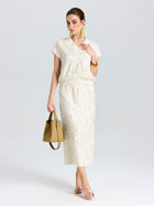 A woman wears the Social Queen Floral Embroidered Linen Top with a matching skirt, tan handbag, sandals, earrings, and bracelet, standing against a plain white background.