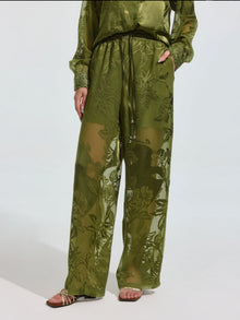 Wearing Social Queen's Botanical Burnout Satin Wide-Leg Pants in olive green with a matching long-sleeve top and sandals, a person stands against a plain light background.