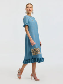 A woman models the Social Queen Beaded Crystal Embellished Dress, featuring a ruffle hem and beaded neckline, paired with a silver handbag, matching heels, and bold earrings.