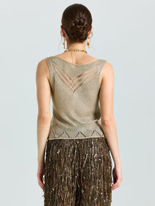 A woman with her hair in a neat bun faces away, wearing the Social Queen Open-Knit Metallic Sleeveless Top paired with a brown sequined skirt featuring geometric cutouts.