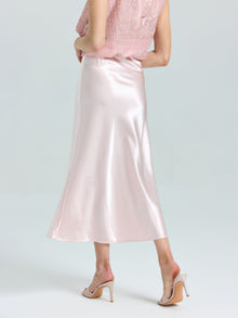 A person wears a light pink lace top, Social Queen's Satin A-Line Midi Skirt in shiny pink, and nude heeled sandals, standing against a plain light background.