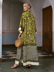 A woman wearing the Social Queen Tropical Fruit Print Linen Dress stands in a hallway, holding a wooden handbag and wearing heeled sandals.
