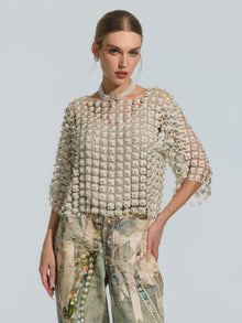 A woman poses against a plain light background wearing the Social Queen Pearl Daisy Cutwork Top (camisole not included), featuring a cropped silhouette embellished with delicate pearl details, paired with printed jeans.