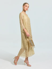 A woman in the Social Queen Pearl Embellished Floral Overlay Dress (Slip Dress Included) with sheer sleeves and pearl accents, holding a gold clutch and wearing strappy heels, stands against a plain background.