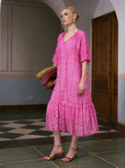 A woman wearing the Social Queen Geometric Jacquard Mulberry Silk Dress and gold sandals stands indoors holding a colorful striped woven bag near a wooden door and tiled floor—perfect for elegant resort wear.