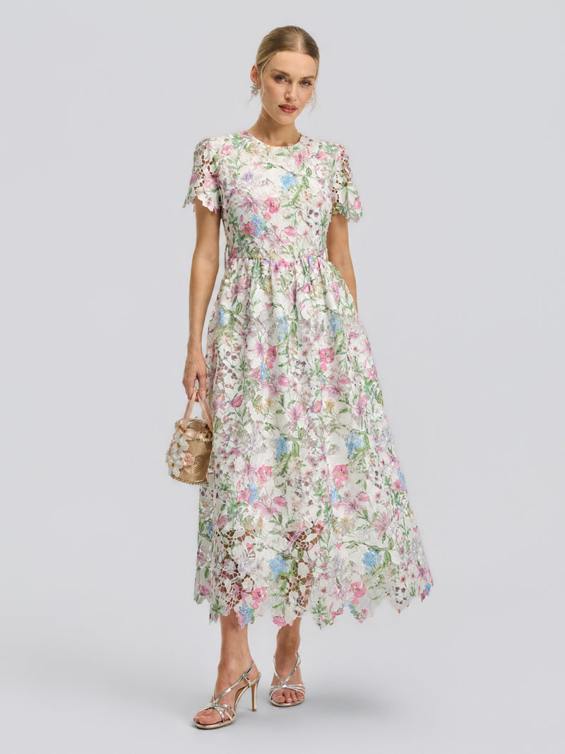 A woman wears the Social Queen Botanical Embroidered Cutout Dress—a white, lace floral A-line dress with short sleeves and a scalloped hem—styled with a small handbag and silver heeled sandals for an effortlessly elegant special occasion look.
