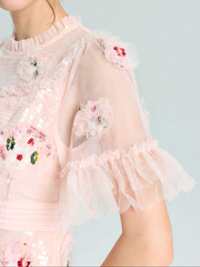 A person wearing the Embroidered Ruffle Tiered Tulle Dress by Social Queen, featuring sheer ruffled sleeves and floral sequin embroidery—an elegant choice for any special occasion.